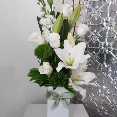 A tall arrangement of white flowers in a tall white vase.