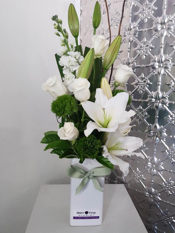 A tall arrangement of white flowers in a tall white vase.