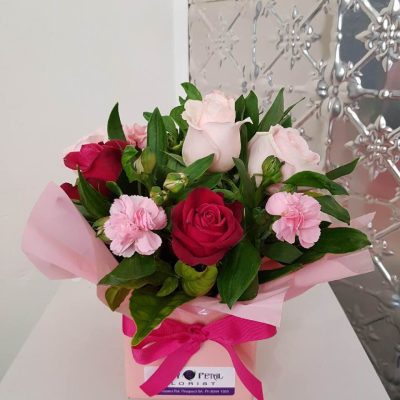 A short arrangement of flowers in a pink box