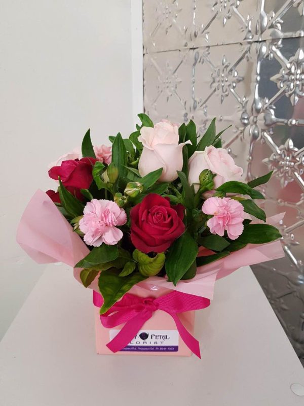A short arrangement of flowers in a pink box