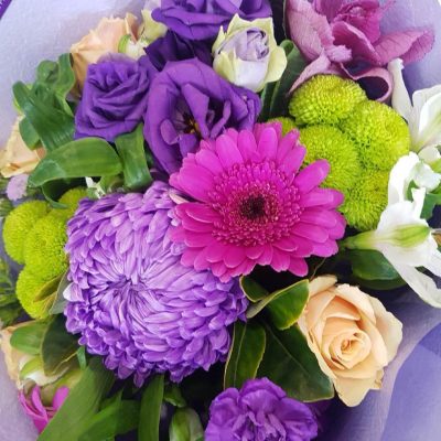 A bouquet of purple flowers wrapped in purple tissue paper.