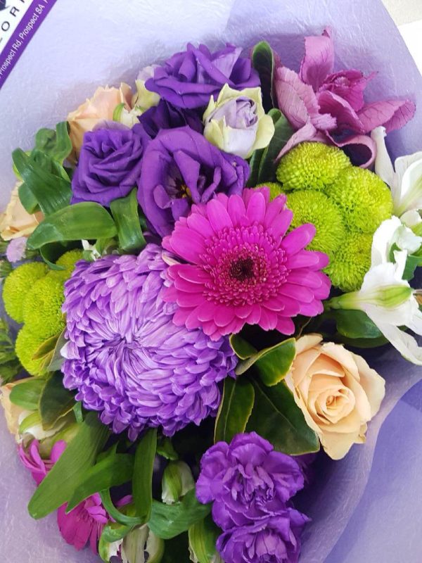 A bouquet of purple flowers wrapped in purple tissue paper.