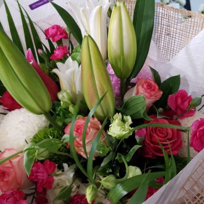 A close up of a bouquet of lilies, roses and carnations wrapped in tissue paper and hessian