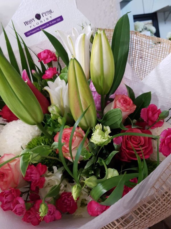 A close up of a bouquet of lilies, roses and carnations wrapped in tissue paper and hessian