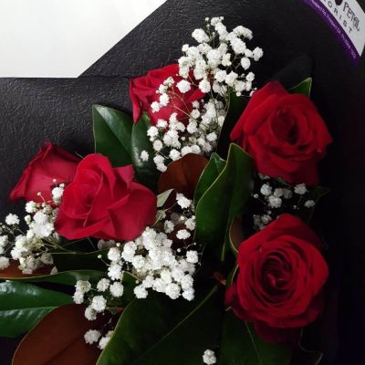 A close up of red roses and baby's breath wrapped in black tissue paper.