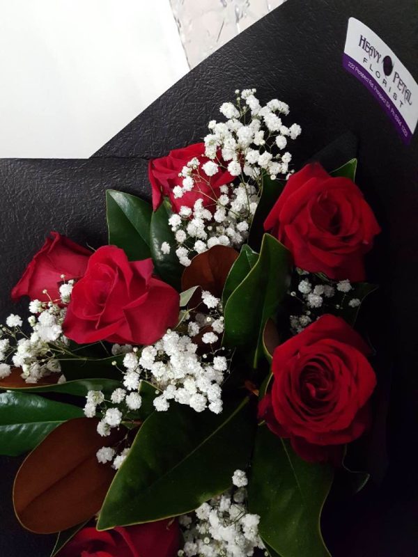 A close up of red roses and baby's breath wrapped in black tissue paper.