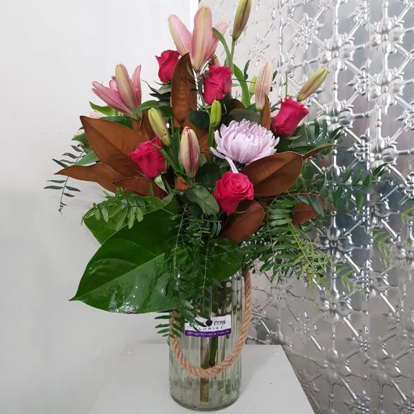 A large bouquet of lilies and roses with green foliage in a rustic vase