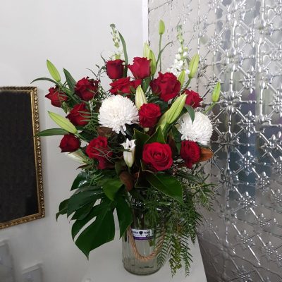 A bouquet of roses and lillies with green foliage in a large rustic vase