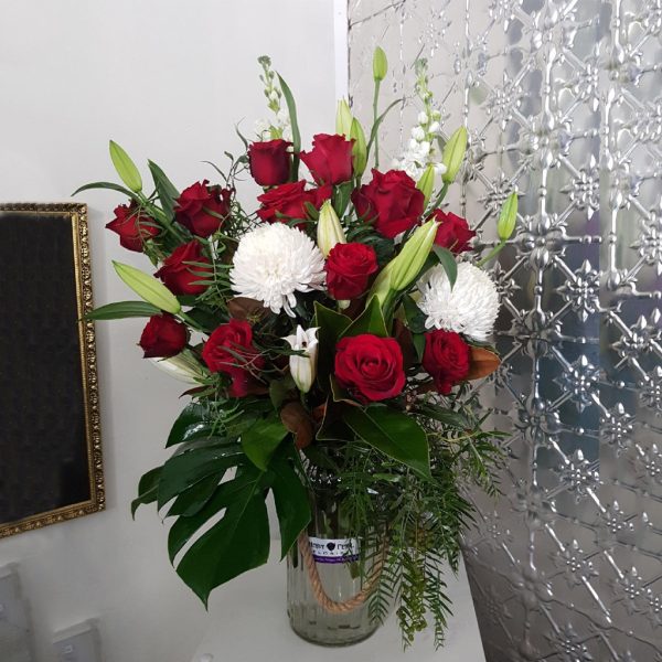 A bouquet of roses and lillies with green foliage in a large rustic vase